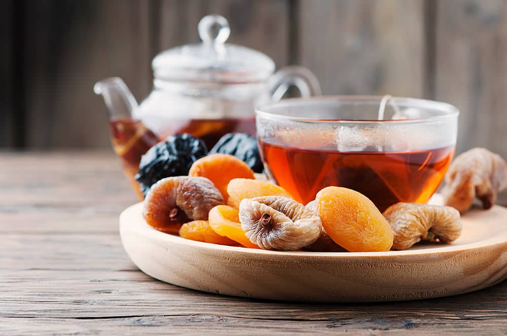 Suszone owoce na talerzyku drewnianym obok filiżanki herbaty.