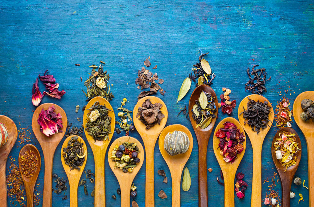 Liście różnych rodzajów herbat rozsypane na drewnianych łyżkach kuchennych.